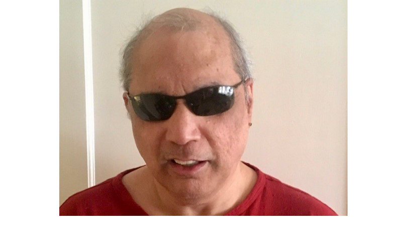Image shows Allan in a red t-shirt and dark glasses he is facing the camera smiling