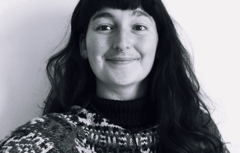 Debbie looks into the camera she has long wavy hair and a big smile she wears a thick wolly jumper 