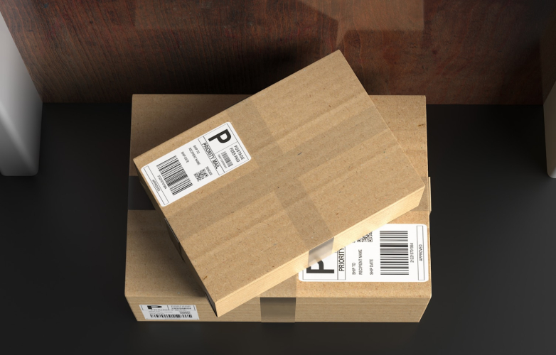One small brown package on top of a large brown package seen from above They are on a black floor outside a brown apartment door