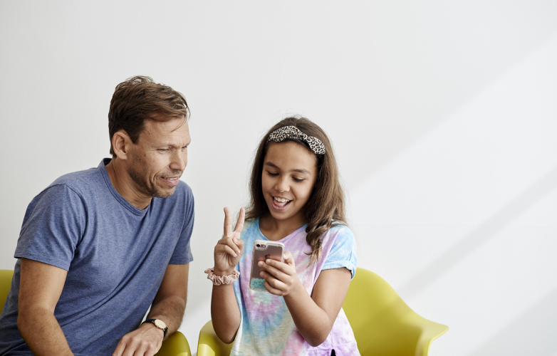 A man and a young girl speaking in sign language and looking at a mobile phone