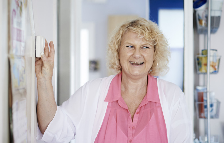 Smiling woman adjusts wall-mounted heating controls